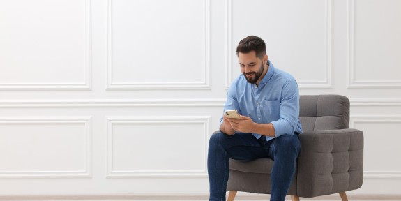 Mann mit Bart sitzt in einem Sessel und schaut in sein Handy
