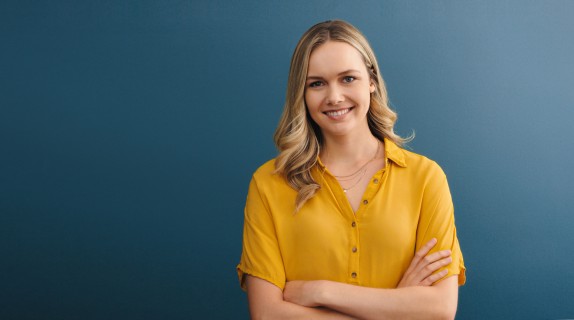 Blonde Frau mit gelber Bluse lächelt vor blauem Hintergrund